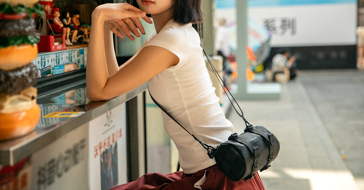 Woman in white top and red pants carrying a black Mark Ryden anti-theft crossbody bag with adjustable strap at a Florence outdoor café.