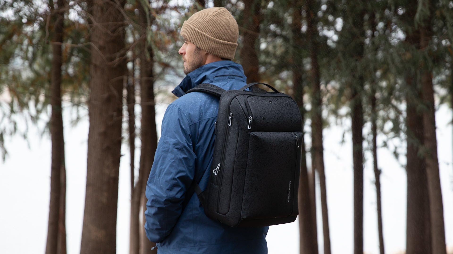 Mark Ryden waterproof black backpack on traveler in blue jacket, rainy forest
