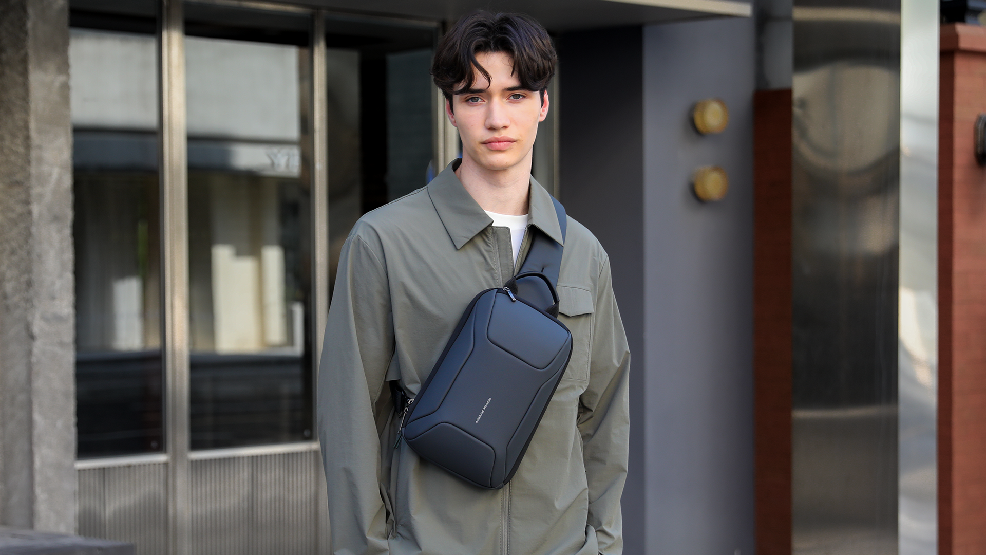 Dark blue Mark Ryden anti-theft crossbody bag with sleek design, worn by a person in a green jacket.