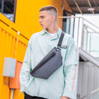 Gray chest bag with black strap on man in light green shirt at urban setting | MarkRyden Global