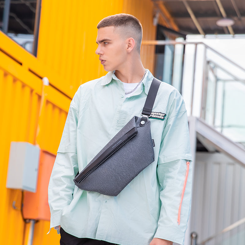 Gray chest bag with black strap on man in light green shirt at urban setting | MarkRyden Global