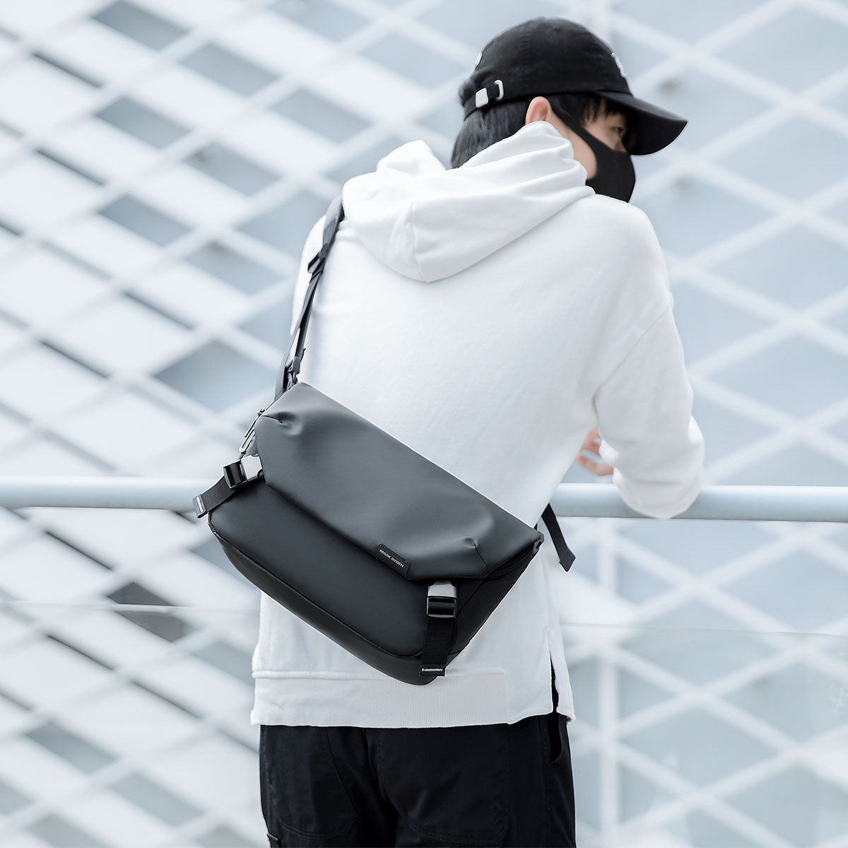 Mark Ryden Global: Black leather waterproof messenger bag on person in white hoodie