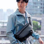 Casual II black leather waterproof scratch-resistant stylish messenger bag worn by a person in a light blue jacket against an urban backdrop.