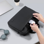 Black MarkRyden Classic IV Tech Commuter Computer Briefcase 14/15.6 inch with hands placing a mouse into a front pocket, surrounded by headphones and a laptop on a desk.