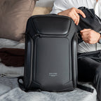 Black Mark Ryden anti-theft backpack with sleek design, zippers, and someone placing a jacket into it—comfortable and versatile for daily and travel use.