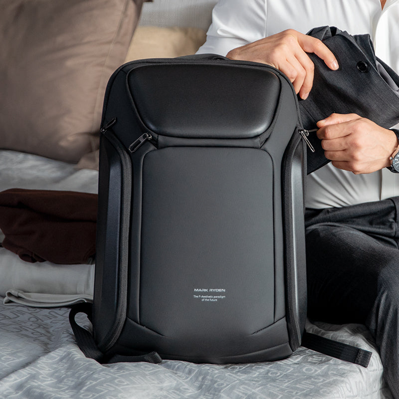 Black Mark Ryden anti-theft backpack with sleek design, zippers, and someone placing a jacket into it—comfortable and versatile for daily and travel use.