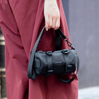 Hand holding Mark Ryden black cylinder crossbody bag with strap