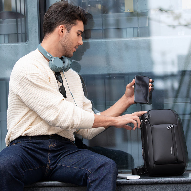 Mark Ryden Global black high-capacity crossbody bag with commuter using it near glass building