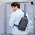 Mark Ryden Global's dark gray high-capacity crossbody bag with zippers, worn by man in light blue jacket outdoors.