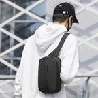 Stylish waterproof black crossbody bag with multiple compartments worn by man in white hoodie near modern building