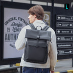 Man in beige coat wears Mark Ryden Global black minimalist backpack at city transit
