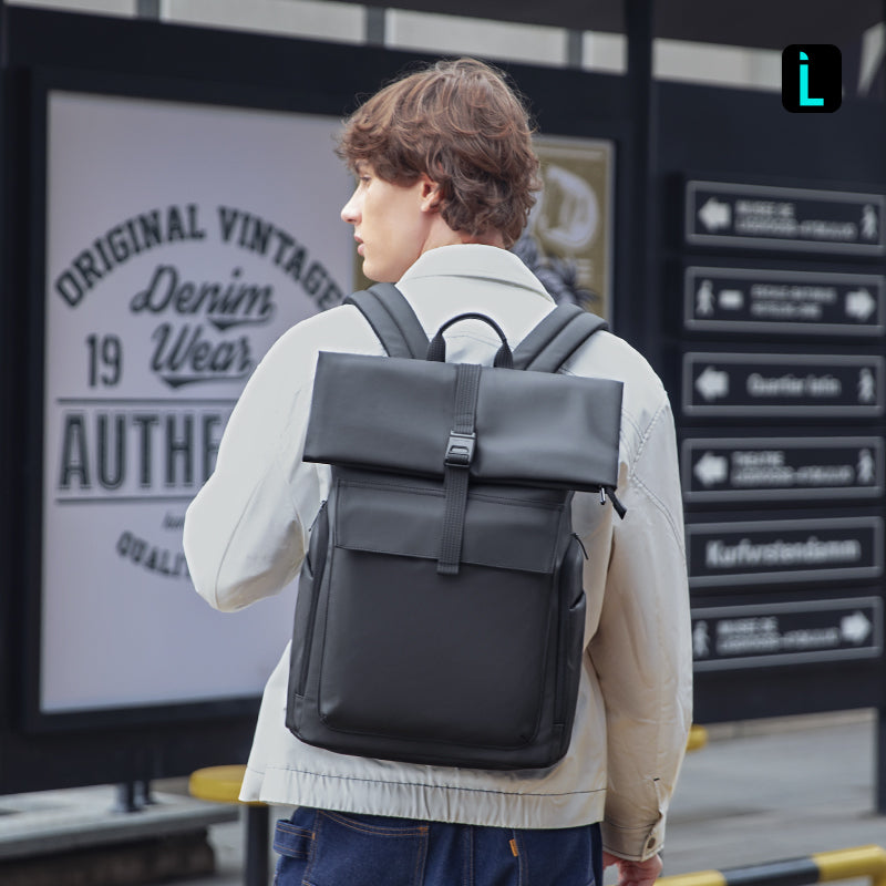 Man in beige coat wears Mark Ryden Global black minimalist backpack at city transit
