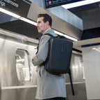 Mark Ryden Global's All-in-One black hard-shell backpack with sleek rectangular design, worn by a man in a subway station, ideal for work and daily commuting.