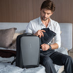 The Ratio Arc Apex All-in-One Hard-shell Backpack in gray and black, with a man packing a suit into it for work.