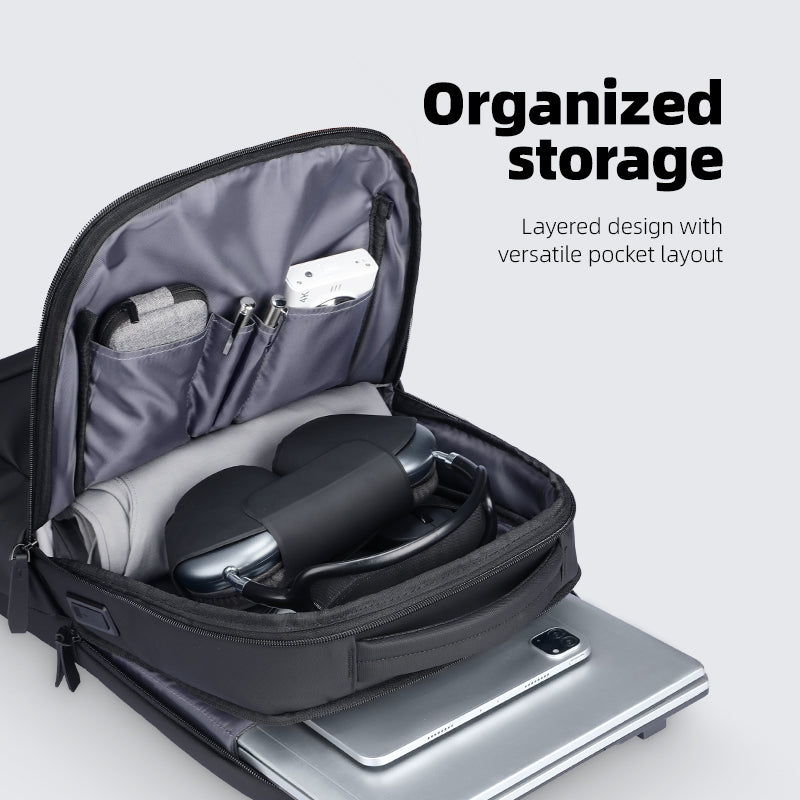 Black lightweight UrbanFlex Lite backpack with open main compartment displaying organized storage: laptop, headphones, and multiple pockets for business essentials.