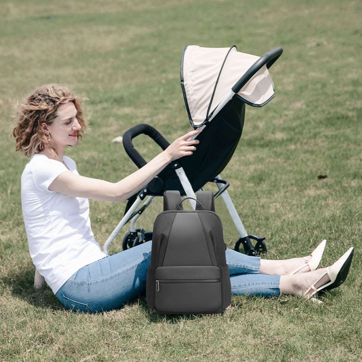 Dark gray Softologic I backpack, water-repellent and organized, placed on grass beside a stroller in a park with a woman sitting nearby.