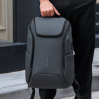 Dark gray waterproof backpack with built-in USB port for travel, held by a person in black pants.