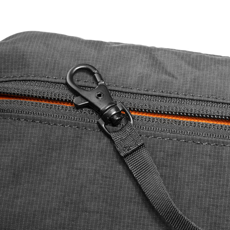 Close-up of dark gray AeroSling ultra-light anti-theft crossbody bag with black carabiner attached to orange-accented zipper, textured fabric, and RFID-Safe technology.
