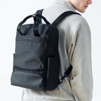 Black Mark Ryden BreezePack lightweight backpack with removable shoulder straps, worn by a person in a gray sweater, featuring front and bottom zippered compartments.