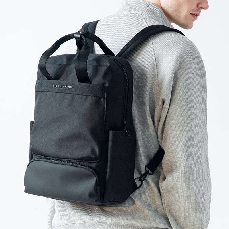 Black Mark Ryden BreezePack lightweight backpack with removable shoulder straps, worn by a person in a gray sweater, featuring front and bottom zippered compartments.