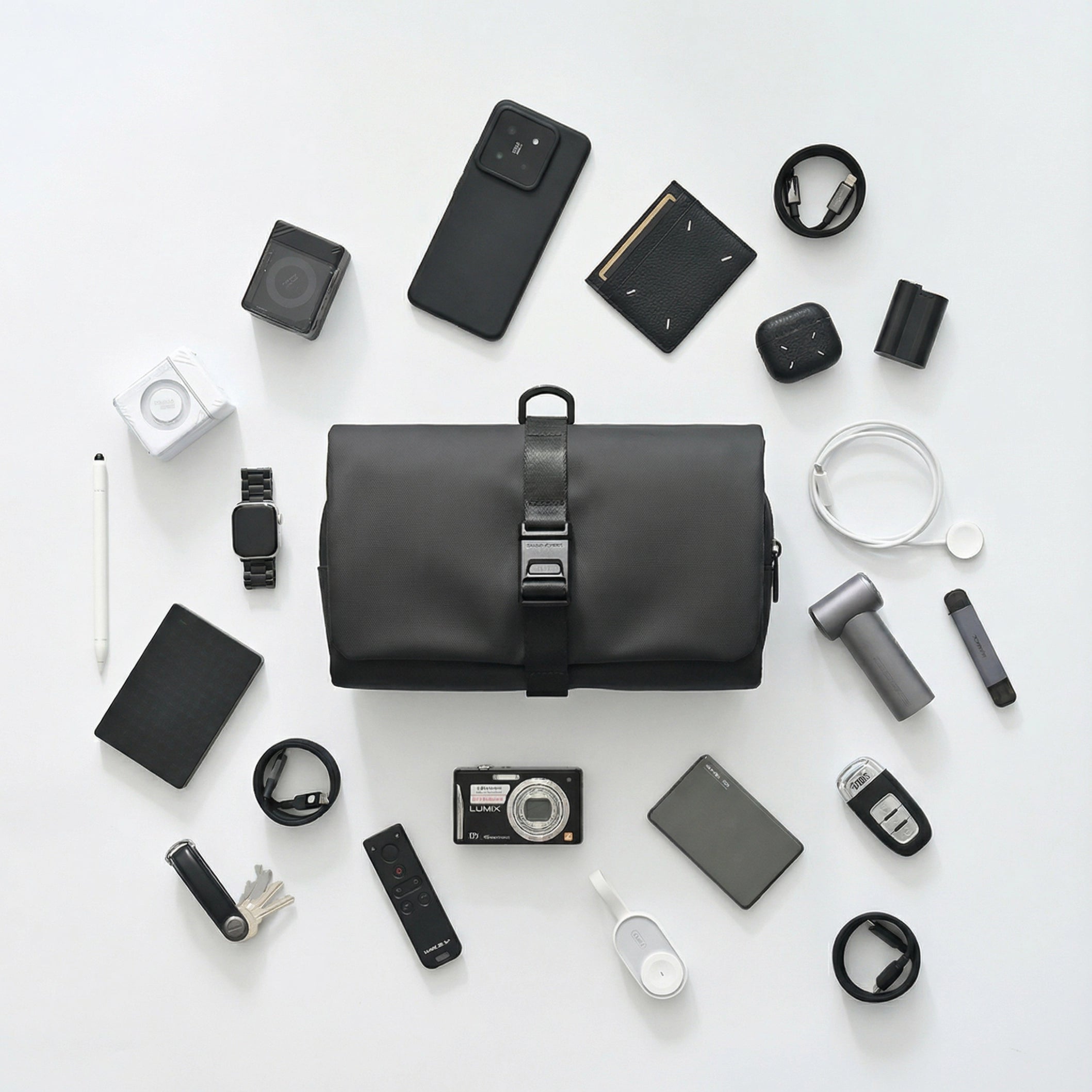 Black MagiClip wet-dry separate toiletry bag with toothbrush holder, featuring a buckle strap, displayed among travel essentials like phone, wallet, and watch.