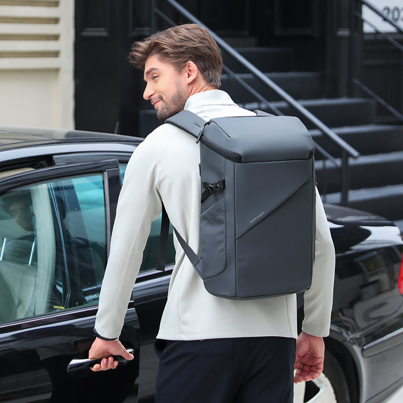 Dark gray AeroShield 2025 durable waterproof backpack with sleek angular design, worn by man near black car in urban setting.